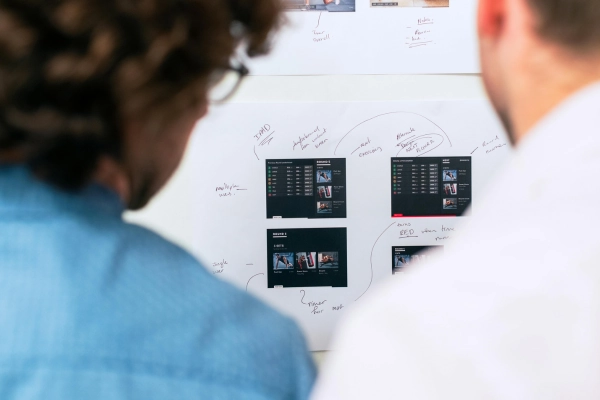 Two people reviewing an app design mockups and notes on a whiteboard