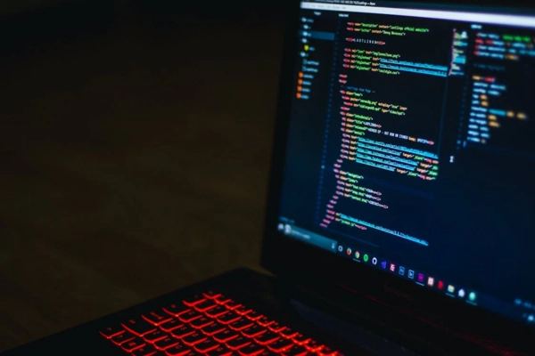 Close-up of a laptop with a red-backlit keyboard displaying code on the screen in a dimly lit room