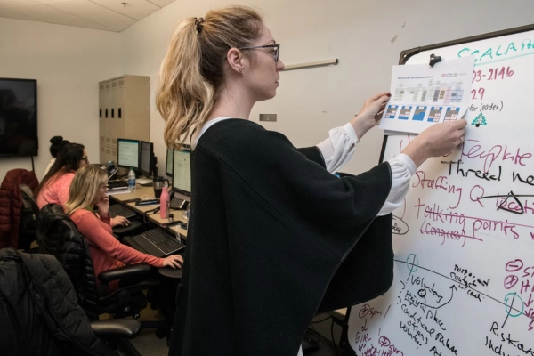 A fractional CTO analyzing data on a whiteboard while colleagues work on computers in the background