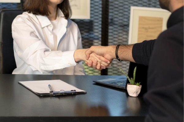 Close-up of a handshake between two people sitting at a desk during a job interview