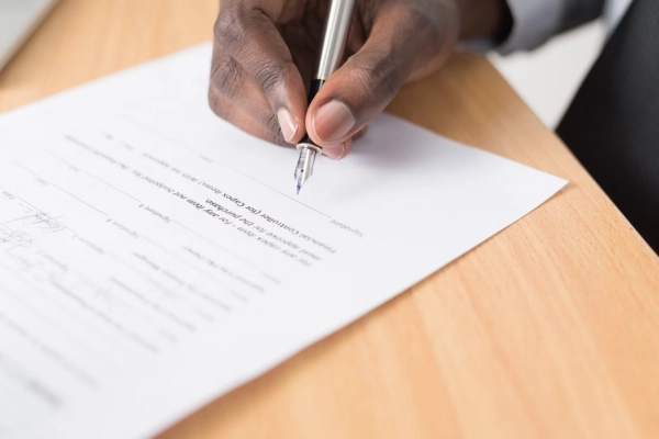 Person signing a contract on a wooden desk