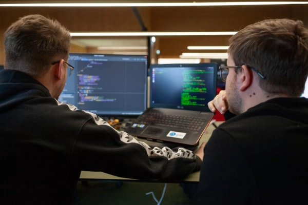 Two developers collaborating while reviewing code on laptop and desktop screens