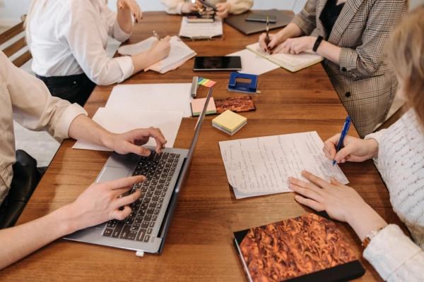 Group of professionals collaborating around a wooden table with notes and laptops