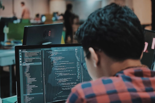 Developer focused on writing code on dual monitors in a team workspace
